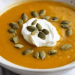 Bol de soupe de potiron avec des graines de courge et crème fraîche dans une cuisine.