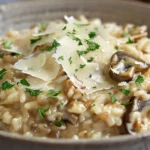 Bol de risotto aux champignons des bois et parmesan, garni de copeaux de parmesan et de persil frais, dans une cuisine de maison