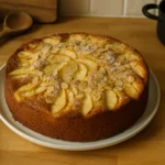 Gâteau aux pommes et amandes moelleux fait maison, photographié dans une cuisine réelle avec des ustensiles autour