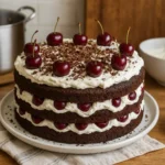 Photo d’un gâteau Forêt Noire traditionnel fait maison avec génoise au chocolat, cerises et crème chantilly, décoré de copeaux de chocolat.