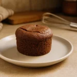 Photo d’un petit gâteau individuel facile, moelleux et fait maison, posé dans une cuisine chaleureuse avec ustensiles en arrière-plan, prêt à être dégusté.