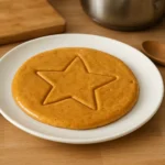 Photo d’un gâteau Squid Game maison en sucre caramélisé, avec une étoile dessinée au centre, posé sur une assiette dans une cuisine familiale.