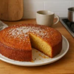 Photo d’un gâteau marocain au miel traditionnel, doré et moelleux, préparé à la maison et nappé de miel, posé sur une table de cuisine marocaine avec des ustensiles rustiques.